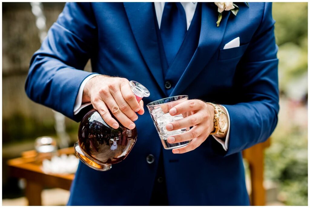 groom pouring glass of bourbon at sapphire creek winery wedding captured by three and eight photography