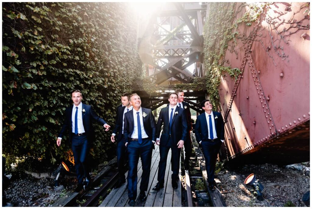 groomsmen walking under bridge on northeast ohio wedding day captured by three and eight photography