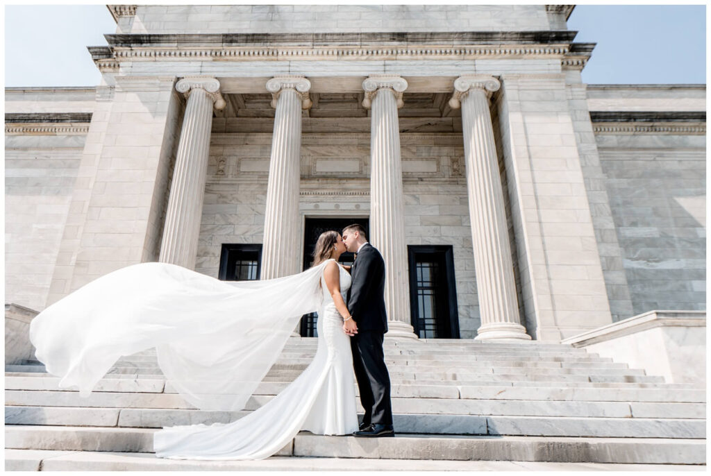 bride and groom kissing on the steps of the Cleveland art museum with cape blowing in the wind