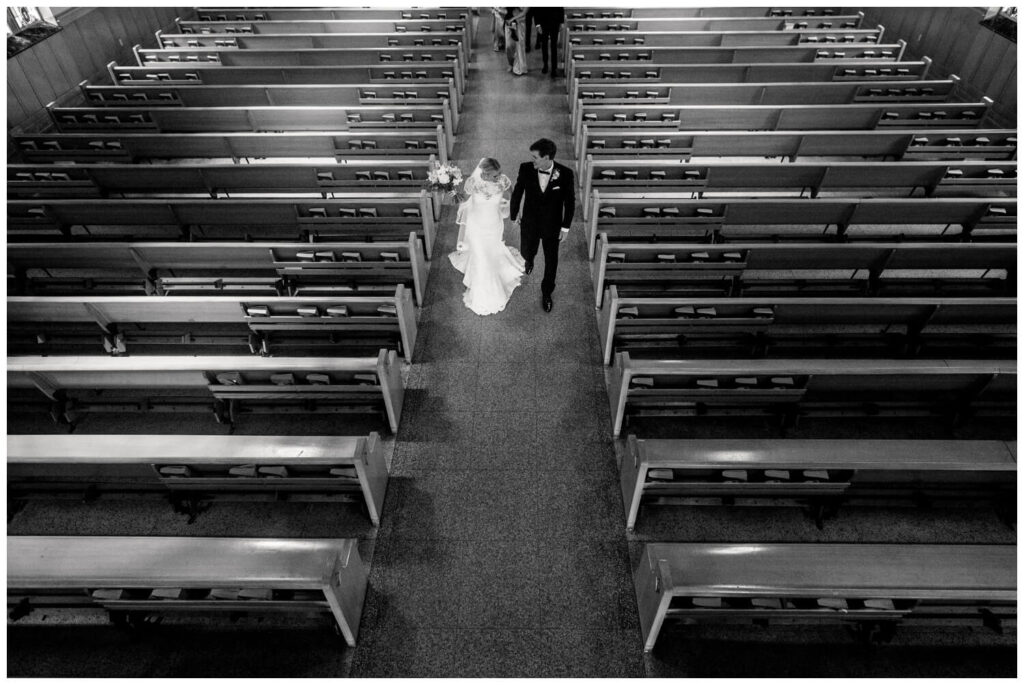 black and white photo of bride and groom walking down aisle in church