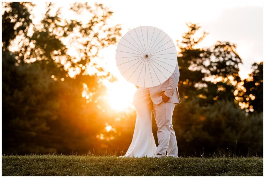 bride and groom hiding behind parasol at sunset at the wellspring in wooster